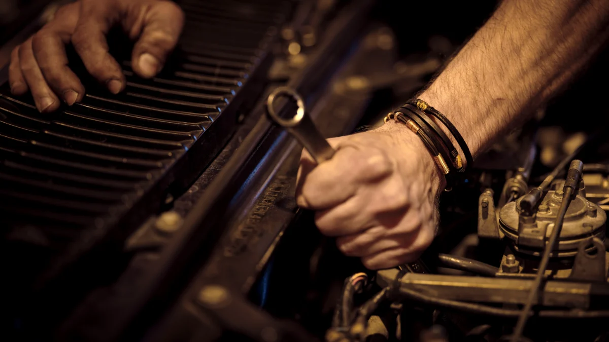 Mechanik pracuje nad silnikiem samochodu w industrialnym otoczeniu, przygotowując go do naprawy, a w tle widoczne są klucze i inne narzędzia