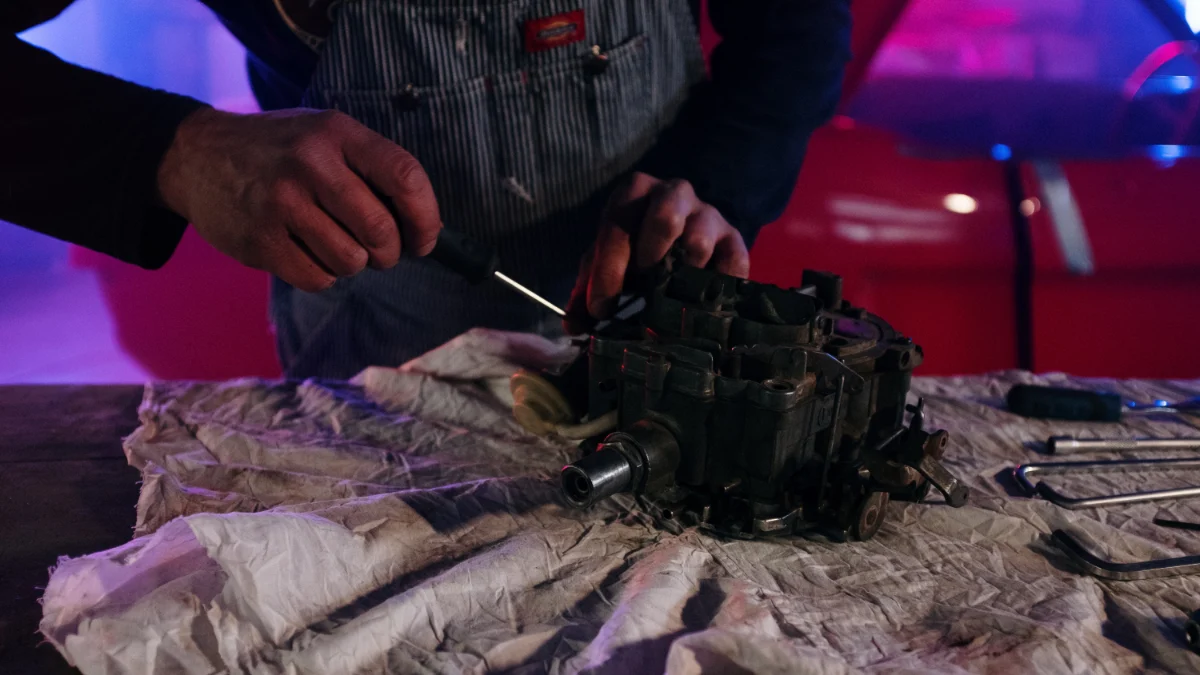 Mechanik naprawiający część do auta vintage w słabo oświetlonym garażu z neonowymi światłami i narzędziami wokół, co wskazuje na