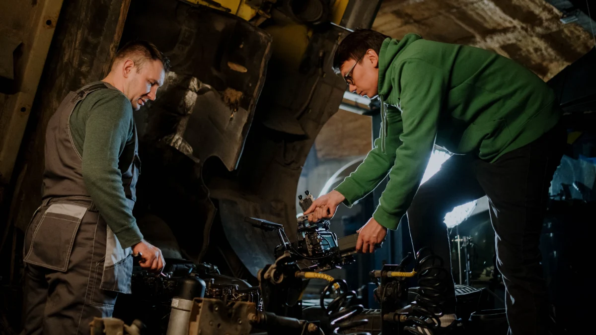 Dwóch mechaników zajętych naprawą silnika w środowisku przemysłowym, wykazujących współpracę