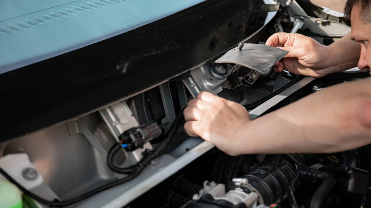 Mechanik pracuje nad silnikiem samochodu na świeżym powietrzu w jasnym świetle dziennym, wskazując na procedurę odłączenia HV, która jest