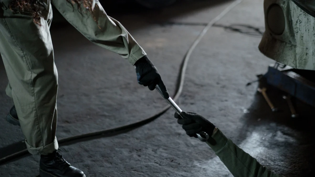 Dwóch mężczyzn w stroju mechanicznym wymieniają klucz w warsztacie, podkreślając współpracę i umiejętności mechaniczne
