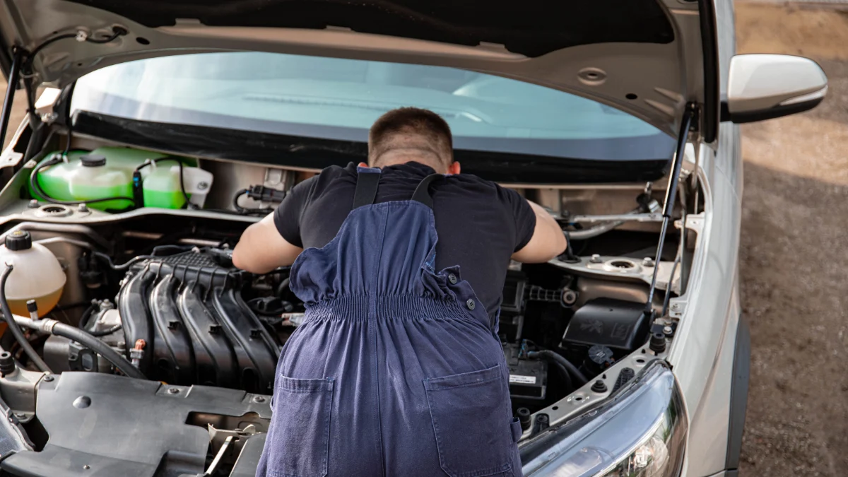 Mechanik w kombinezonie pracuje nad silnikiem samochodu na zewnątrz, oferując usługi naprawy pojazdów