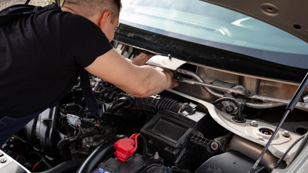 Mechanik zajęty naprawą silnika pod maską samochodu w warsztacie, symbolizujący zastosowanie sieci LIN, FlexRay i Automotive Ethernet w