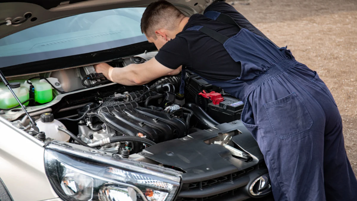 Mechanik koncentruje się na naprawie silnika samochodowego w plenerze, prezentując precyzję, w tym szczegółowy widok mechanicznej pracy