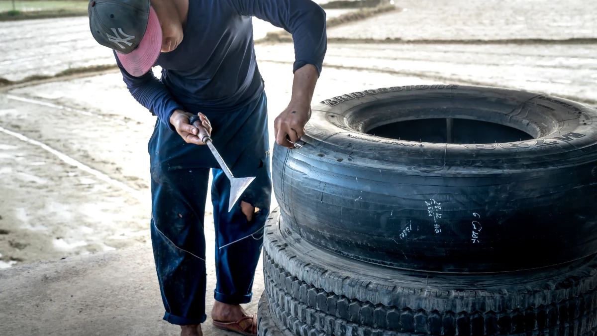 Mężczyzna pracuje nad dużą oponą na zewnątrz, używając narzędzia do napraw, w tym widać wygląd opony, narzędzia mechaniczne i ręce mężczyzny