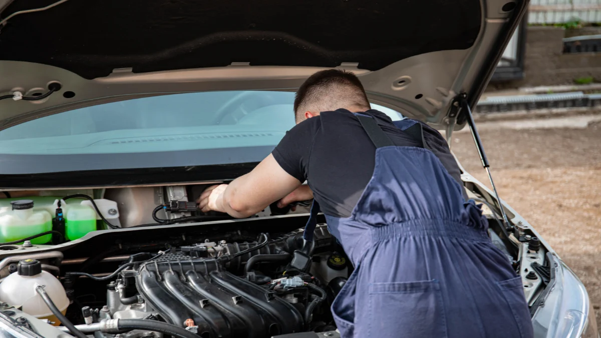 Mechanik naprawia silnik samochodu na świeżym powietrzu w ciągu dnia w warsztacie