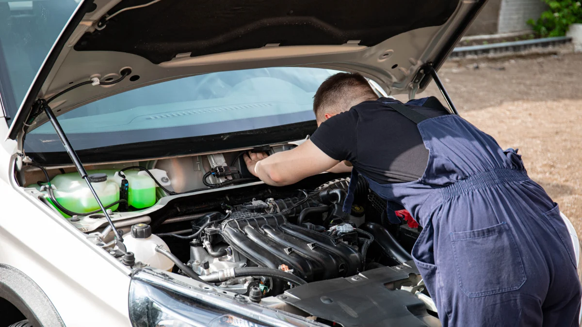 Wykwalifikowany mechanik pracuje nad silnikiem samochodu w plenerze, prezentując konserwację motoryzacyjną, w tym również pompy ciepła w