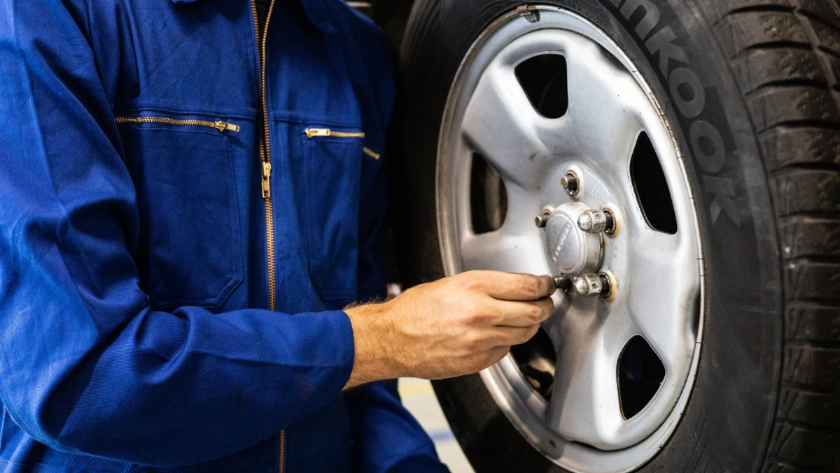 Mechanik w niebieskim kombinezonie sprawdza oponę samochodową w warsztacie naprawczym