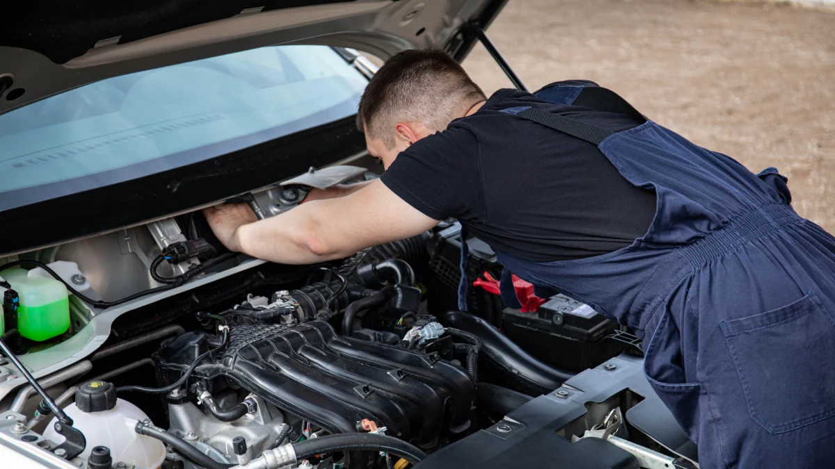 Mechanik w kombinezonie pracuje nad silnikiem samochodowym na zewnątrz, pokazując konserwację motoryzacyjną