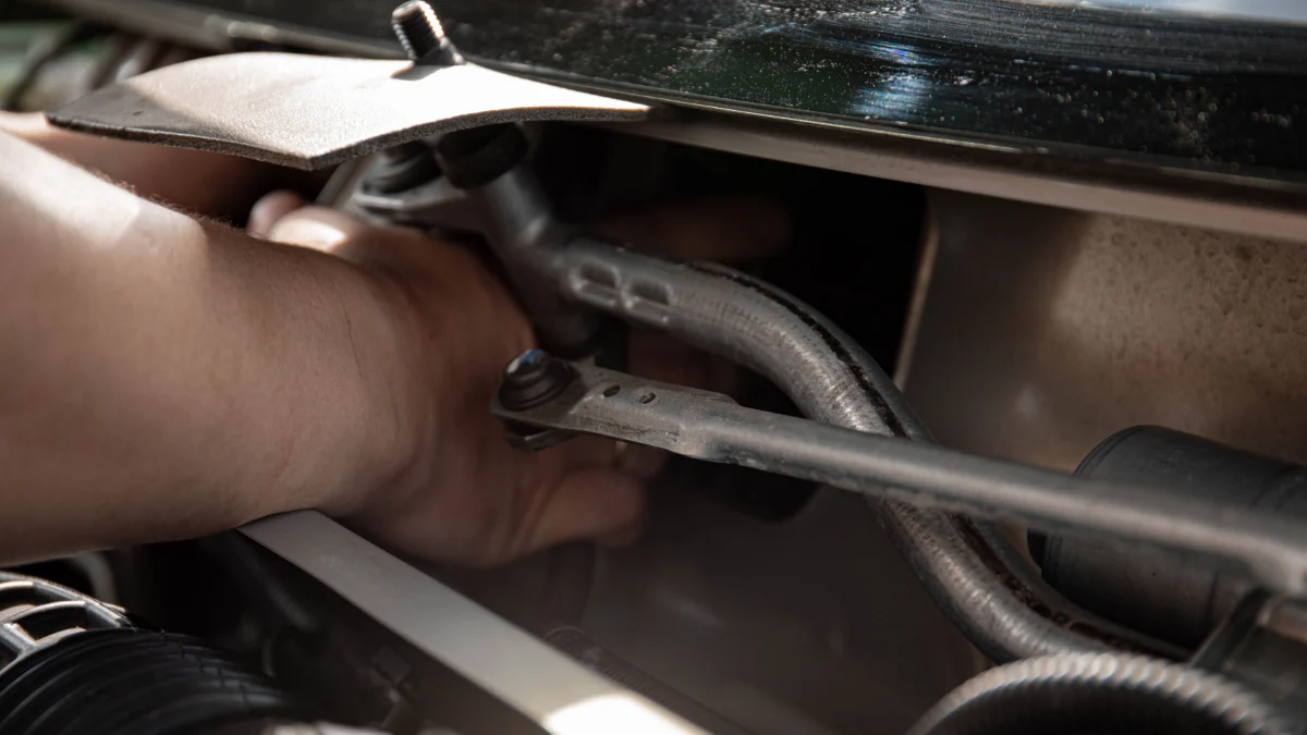 Mechanik naprawiający silnik samochodu, zwrócony w kierunku ręki, z widocznymi narzędziami i maszynami w tle
