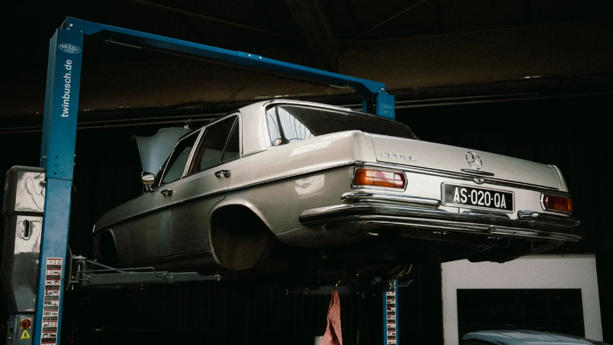 Klasyczny Mercedes-Benz jest przedstawiony w warsztacie samochodowym, w którym można zobaczyć różne elementy takie jak magazyn, tablica z