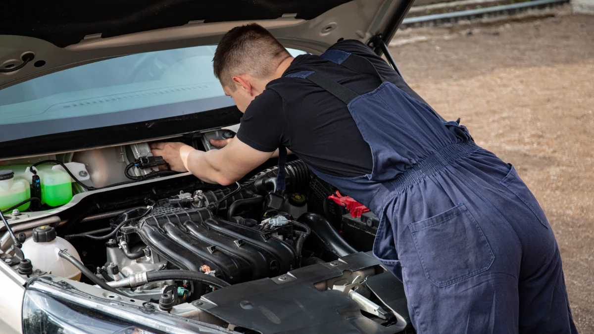 Mechanik w kombinezonie naprawiający silnik samochodu zewnętrznie, prezentujący umiejętności naprawy pojazdów