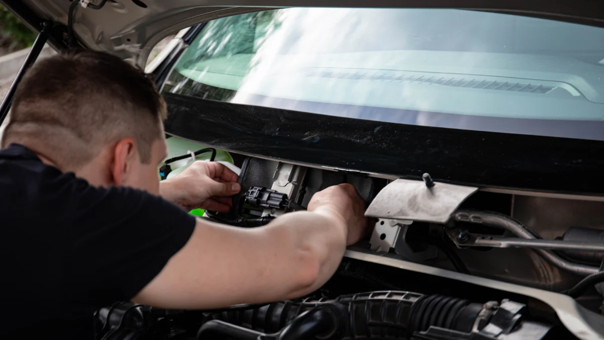 Mechanik pracuje nad komorą silnika samochodu w pomieszczeniu, wykonywając naprawy
